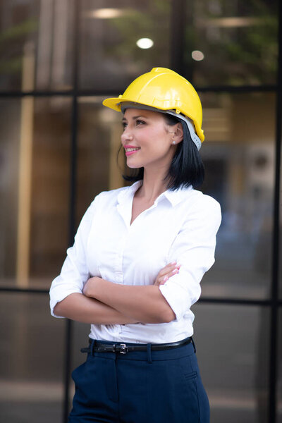 Portrait of Smart Business Woman Civil Engineer and Architecture Wearing Yellow Helmet Hard Hat while Standing and Crossed Arms in Business Building Project with Confidence Poses