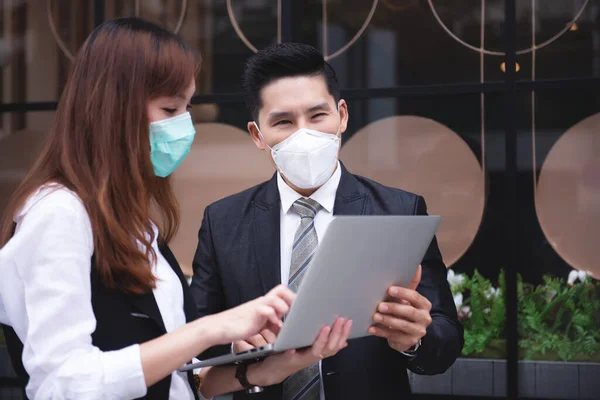 アジアのビジネス関係者が屋外でノートパソコンを操作新ビジネスのビジネス街 彼らはインフルエンザやコロナウイルスを防ぐために保護マスクを着用しています Covid — ストック写真