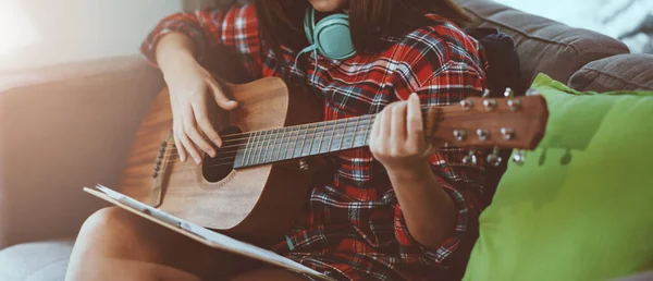 Coronavirus ya da covid-19 salgınında rahatlamak için evde gitar çalan güzel Asyalı genç hippi kız.