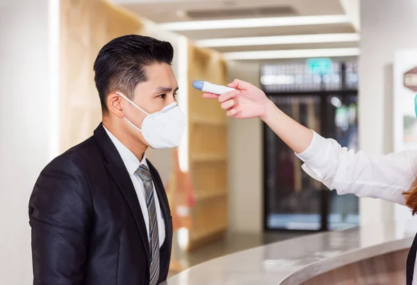 Resepsiyon Operatörü, Ofis Bölgesi 'ne girmeden önce Coronavirus (COVID-19) salgınından korunmak için Dijital Termometrenin ateşini kontrol ediyor - Sağlık Konsepti