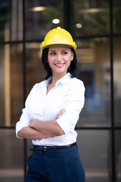 Portrait of Smart Business Woman Civil Engineer and Architecture Wearing Yellow Helmet Hard Hat while Standing and Crossed Arms in Business Building Project with Confidence Poses