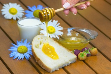 Tahta kaşıktan taze bal damlıyor tatlı ekmek için, bir bardak süt, ahşap masa