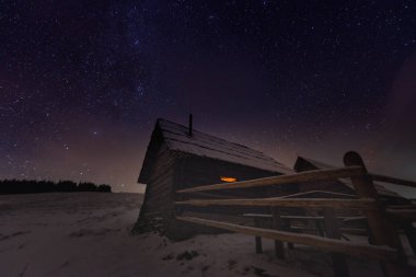 Kış dağları üzerinde görkemli Samanyolu. Gece sahnesi. Penceresinde ışık olan ahşap bir ev. Kukul sırtı, Karpatlar, Ukrayna, Avrupa.