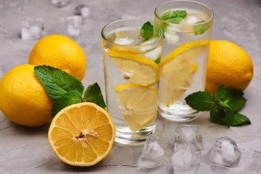 Limonata bardakta servis edilir, portakallı buz küpleri gri masa arkasında.