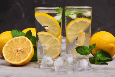 Limonata bardakta servis edilir, portakallı buz küpleri arka planda.