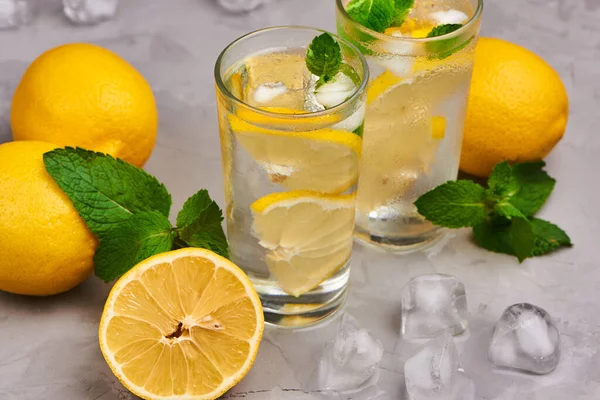 Limonata bardakta servis edilir, portakallı buz küpleri arka planda.