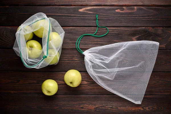 Green apples in mesh bag - eco concept. Brown wooden background