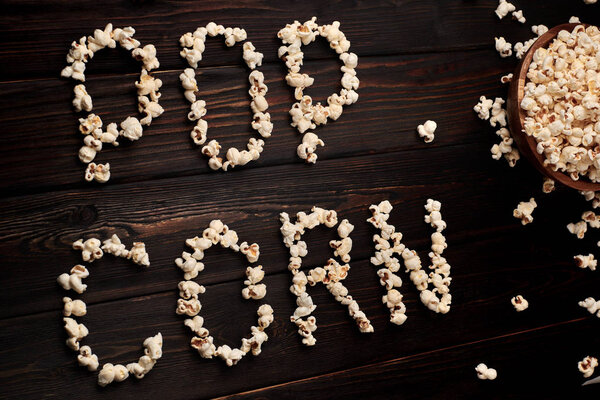 Деревянная чаша с соленым попкорном на деревянном столе. Темный фон. Выборочный фокус. Плоский лежал
