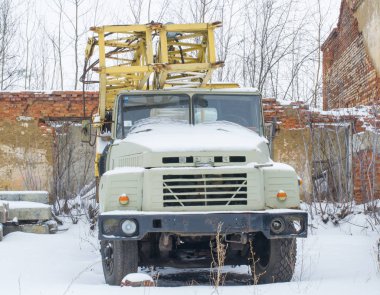 Eski sarı bir Kraz kamyon vinci terk edilmiş tuğla binaların arasında duruyor..