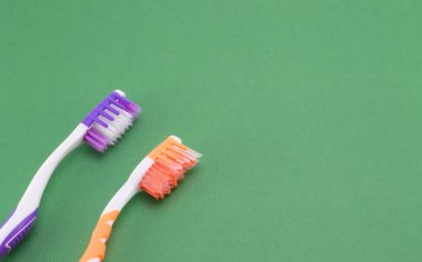 İki diş fırçası. Beyaz-turuncu ve beyaz-menekşe. Yeşil bir arka planda. Başlıkları fırçala