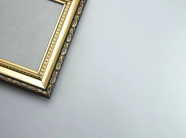 Part of an empty photo frame in black and gold on a light gray plain background. The angle from the frame without a photo.