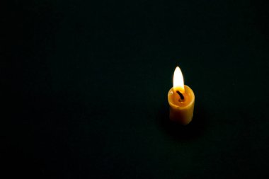 Tamamen karanlıkta, küçük, sarı bir mum. Sağda, siyah arka planda. Mum ışığı üçüncülerin kuralıdır..