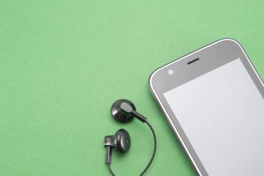 Beyaz kenarlı siyah akıllı telefon (çizgili) daire şeklinde. Gri boş ekran. Ve kulaklıktan kulaklığa yerleştirmek için iki küçük siyah kulaklık. Telefonun yeşil izole bir arkaplanı var.