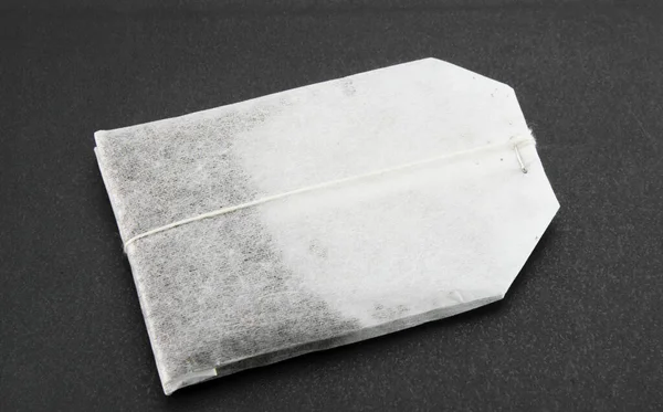 White New Tea Bag Lies Black Textured Background Close — Stock Photo, Image