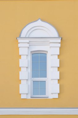 Sarı bir duvarda kemerli, eskimiş beyaz pencere. Güzel mimari. Resmin dibindeki beyaz karelerin çerçevesi bir korteks. Cam üzerindeki dekoratif çizgiler, metal gelgitler.