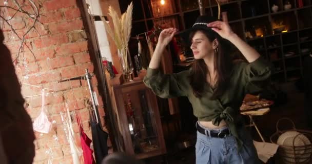 Молодая женщина примеряет шляпу в винтажном магазине — стоковое видео