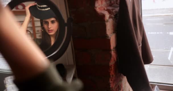 Дзеркальне зображення жінки, що випробовує капелюх у вінтажному магазині — стокове відео