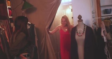 Sarışın kadın butik dükkanında elbisesini arkadaşına gösteriyor.