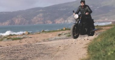 Deniz kenarında klasik motosiklet süren yakışıklı motorcu.