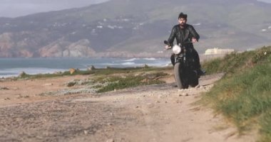 Deniz kenarında klasik motosiklet süren yakışıklı motorcu.