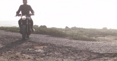 Deniz kenarında klasik motosiklet süren yakışıklı motorcu.