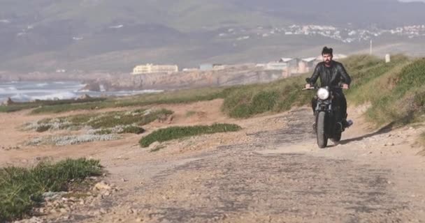 Hombre motero guapo montando motocicleta clásica por el paseo marítimo — Vídeos de Stock