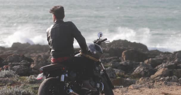 Voltar ver o homem sentado na motocicleta clássica olhando à beira-mar — Vídeo de Stock