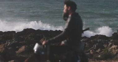 Deniz kenarındaki motosiklette deri ceket giyen yakışıklı adam.