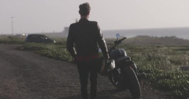 Deniz kenarında motosiklete binen bir adamın arka görüntüsü.