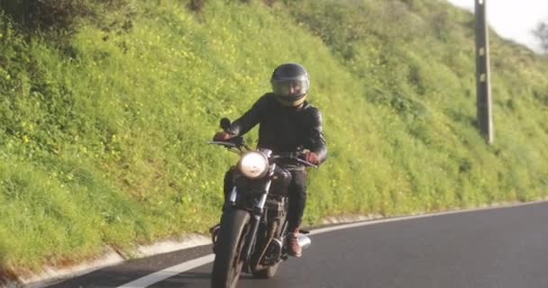Байкер едет на классическом мотоцикле по проселочной дороге — стоковое видео