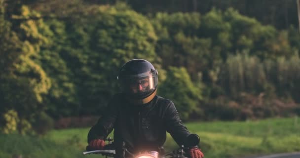 Hombre ciclista montando motocicleta clásica en la carretera del campo durante el atardecer — Vídeo de stock