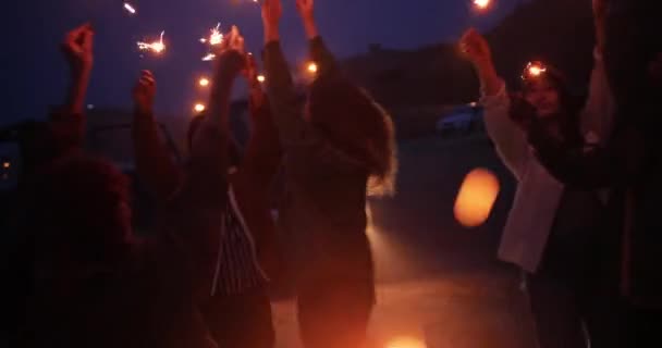 Amigos multiétnicos celebrando y bailando sosteniendo bengalas por la noche — Vídeo de stock