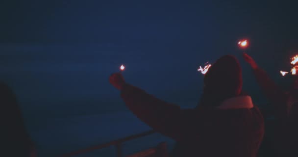 Gruppo multietnico di amici che tengono scintille sulla spiaggia di notte — Video Stock