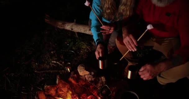 Close-up van senior paar eten marshmallows door de vreugdevuur — Stockvideo