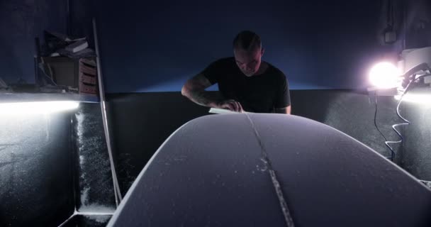 Man shaping surfboard with sanding block in workshop — Stock Video