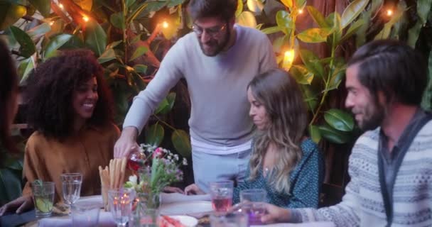 Man serveert wijn aan multi-etnische vrienden tijdens de maaltijd op de patio — Stockvideo