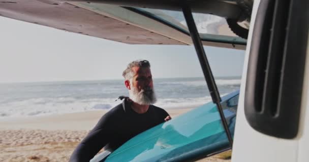Uomo anziano bello che rimuove la tavola da surf dal furgone in spiaggia — Video Stock