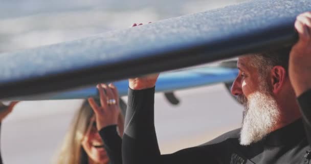 Крупним планом старший чоловік і жінка, що несе дошки для серфінгу над головою — стокове відео