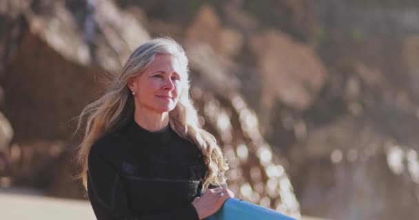 Закрыть пожилую красивую женщину, держащую доску для серфинга на пляже — стоковое видео
