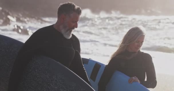 Cerca de hombre y mujer senior llevando tablas de surf en la playa — Vídeos de Stock