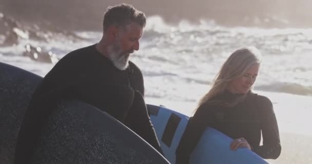 Närbild senior man och kvinna som bär surfbrädor på stranden — Stockvideo