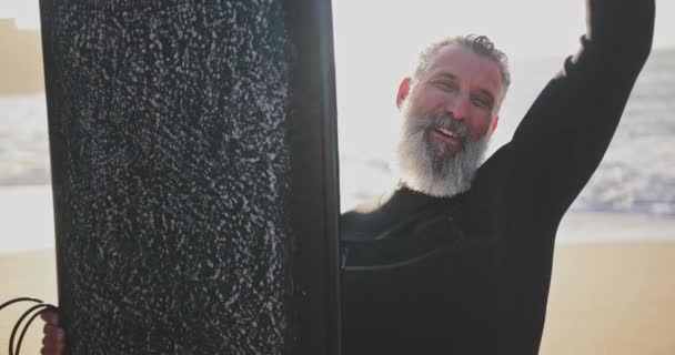 Κοντινό πλάνο ανώτερος άνθρωπος χαμογελά κρατώντας σανίδα του σερφ στην παραλία — Αρχείο Βίντεο
