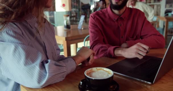 Cerca de la mujer rubia y el hombre de Oriente Medio utilizando el ordenador portátil en la cafetería — Vídeos de Stock