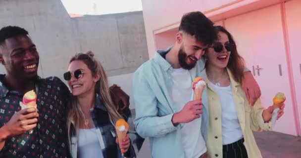 Close-up multi-ethnic friends eating ice creams walking by pink building — Stock Video