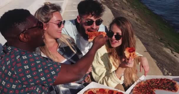 Cerca de amigos multiétnicos comiendo pizza para llevar a orillas del río — Vídeo de stock