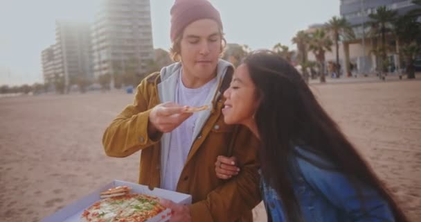 Unga multietniska par som har kul med att äta pizza på stranden — Stockvideo