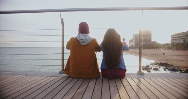 Feliz pareja de adolescentes comiendo helado y sentados en un embarcadero de madera — Vídeos de Stock