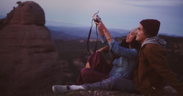 Multi-ethnic hipster couple with camera taking selfies on mountain peak — Stock Video