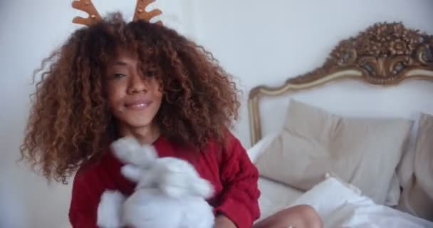 Чорна жінка грає з плюшевою іграшкою, сидячи хрестоподібною на ліжку — стокове відео