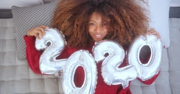 Black woman lying on a bed holding 2020 balloons — Stock Video